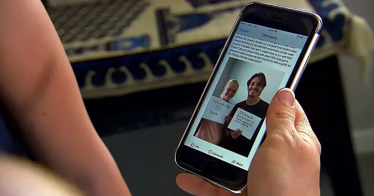A hand holds an iPhone displaying a Facebook post seeking help to find twin sisters born in Florida.