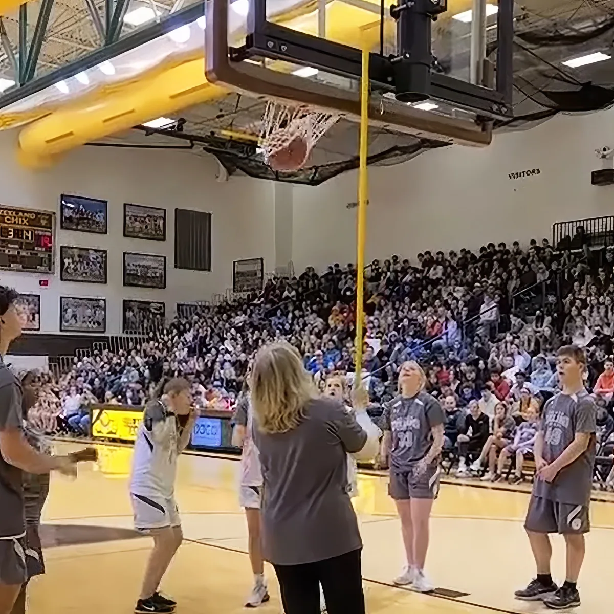 A basketball player in a white jersey is about to shoot the ball while a coach and a referee watch in a gymnasium filled...