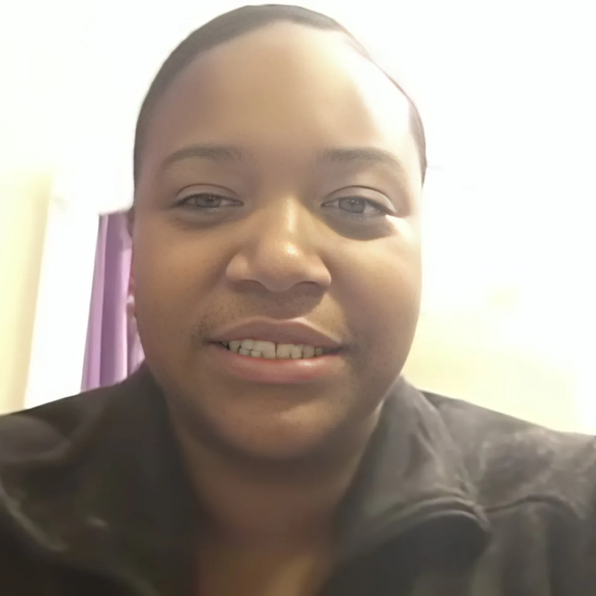 A person wearing a dark jacket smiles in a close-up shot with a blurry background.
