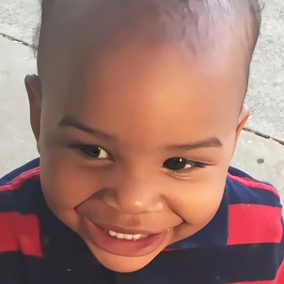 A smiling child with short hair, wearing a striped shirt, looking directly at the camera.