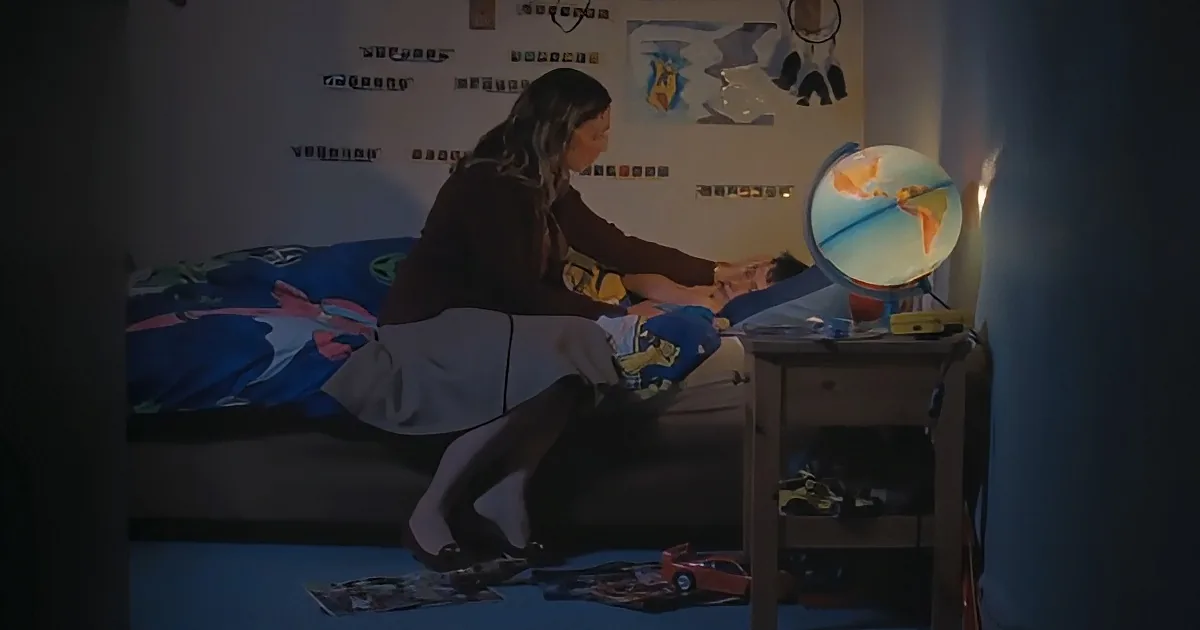 A person sits on a bed, interacting with a globe on a small table in a dimly lit room.