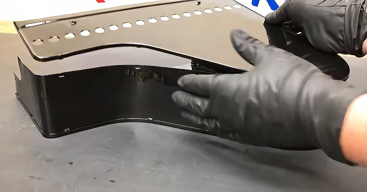 A person in black gloves holds a shiny, curved metal object with holes on top.
