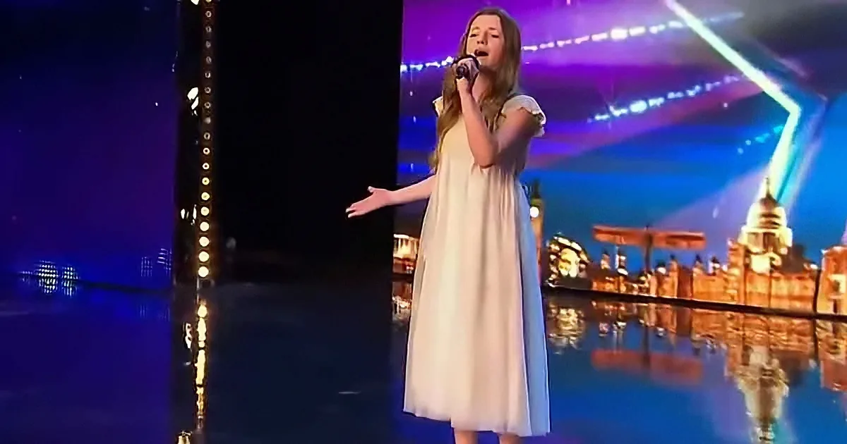 A girl in a white dress sings on stage with a cityscape backdrop and colorful lights.