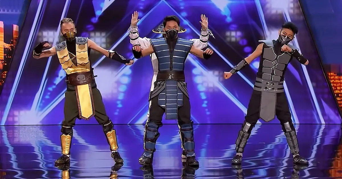 Three individuals in Mortal Kombat-inspired costumes perform on a stage with a cityscape backdrop.