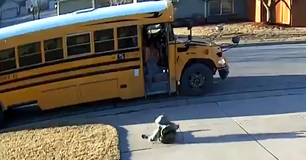 A school bus with its door open and a person lying on the sidewalk nearby.