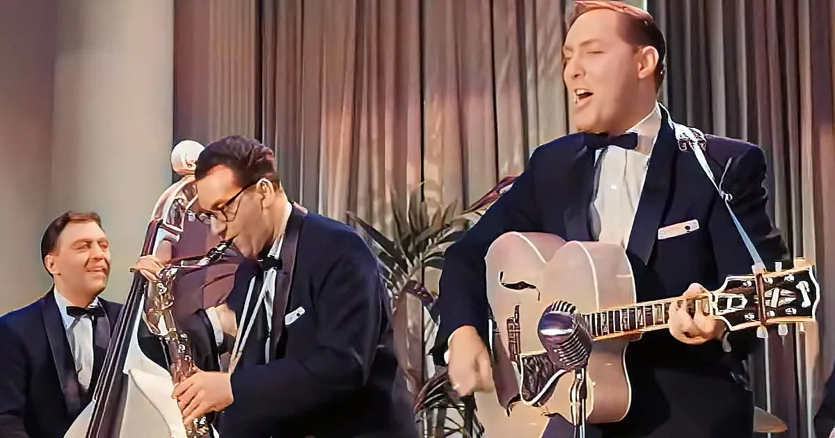 A man in a suit plays guitar and sings into a microphone on stage.