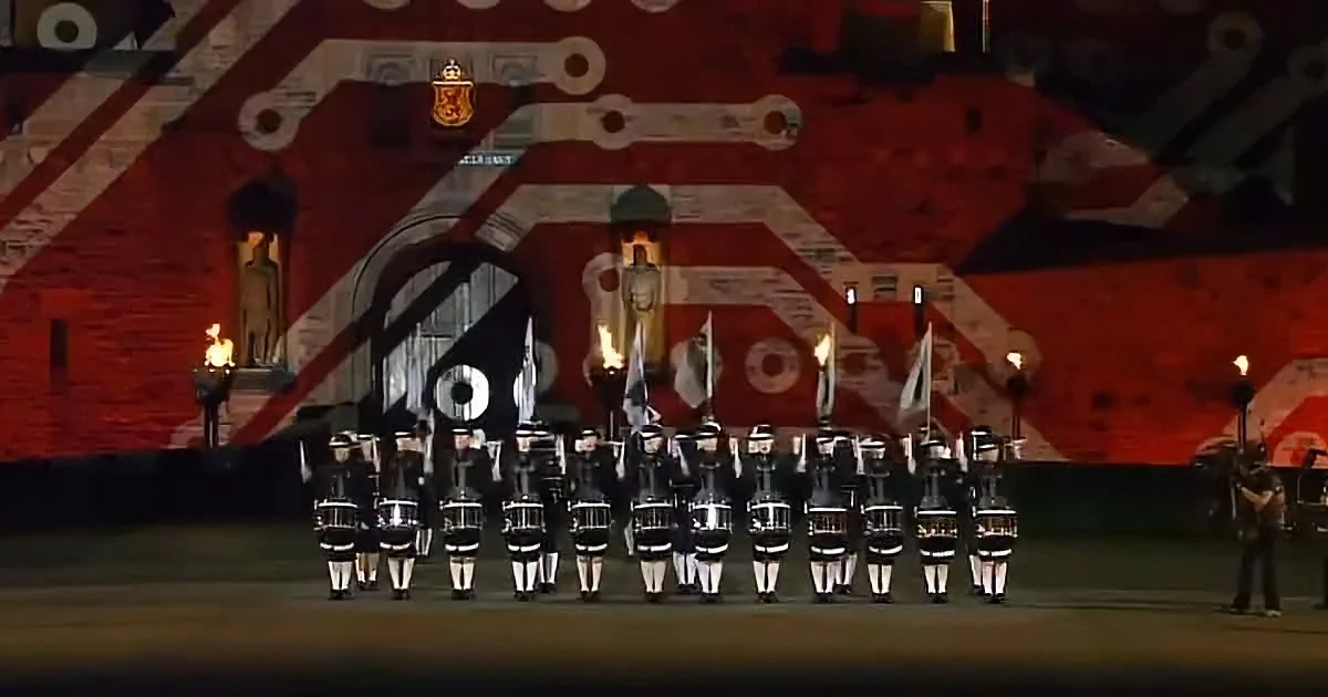 A ceremonial parade with soldiers in uniform marching in formation, holding flags and torches, against a backdrop of a...