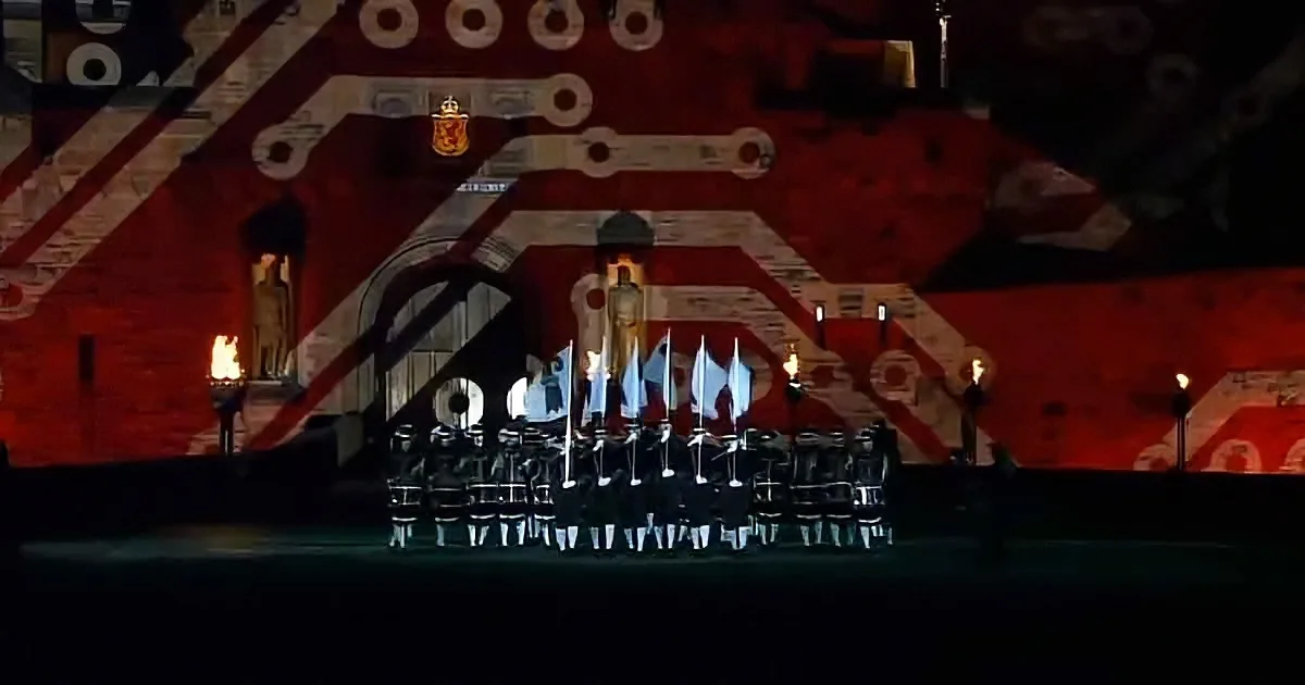 A ceremonial scene with soldiers in uniform holding flags, flanked by torches, against a backdrop of red and white...