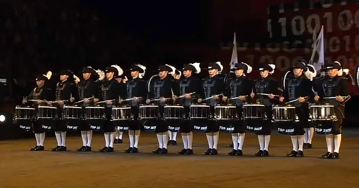A marching band in kilts and hats plays drums in a line formation.