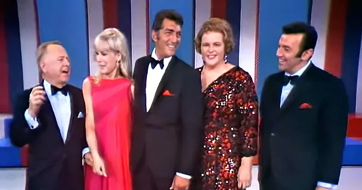 A group of five people in formal attire stands together on a stage, smiling and laughing.