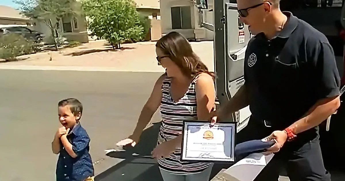A woman receives a certificate from a man in uniform, watched by a child.