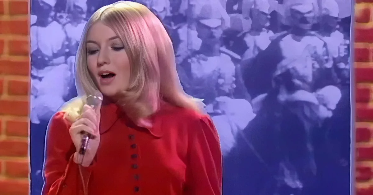 A woman in a red outfit sings into a microphone, with a blurred crowd in the background.