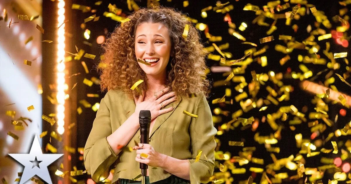 A woman with curly hair, wearing a green blazer, holds a microphone and smiles amidst falling gold confetti.