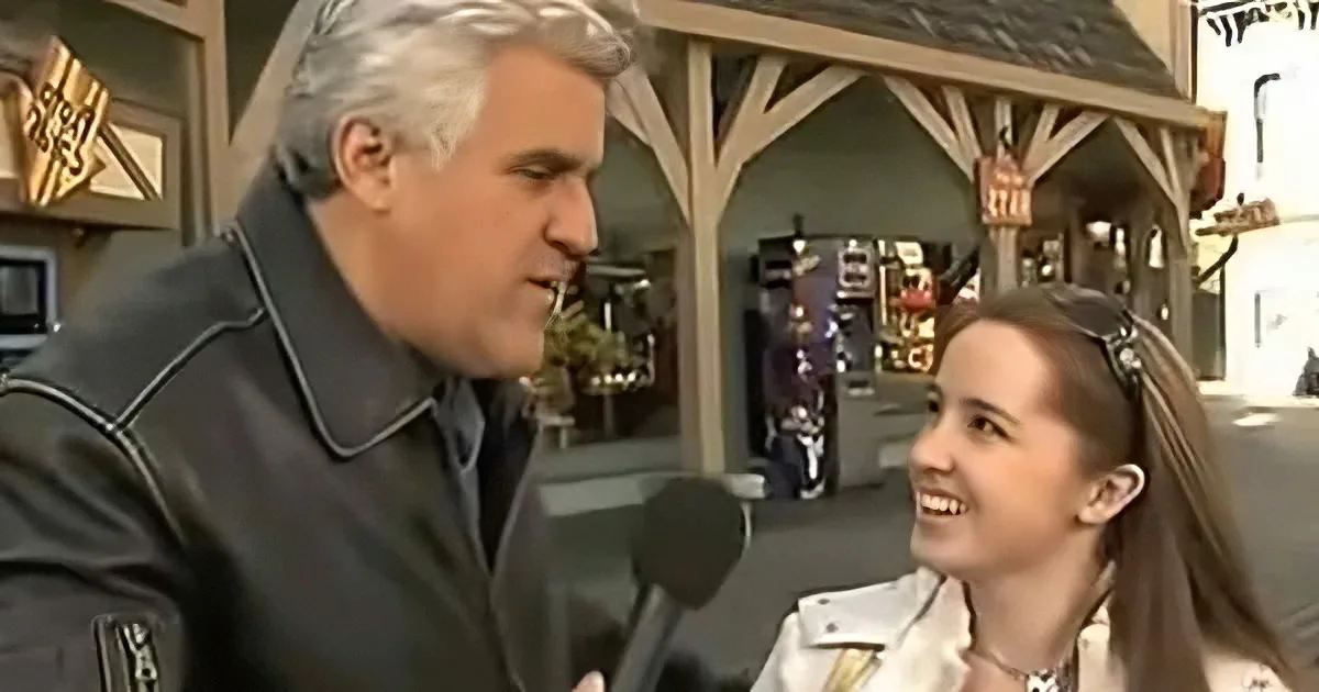 A man in a black jacket is holding a microphone, interviewing a smiling woman with long hair.