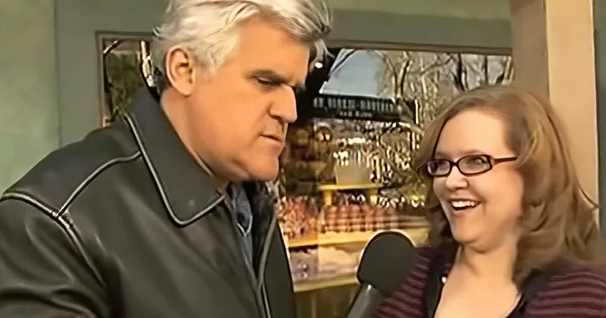 A man in a black jacket and a woman in a striped shirt are engaged in conversation, with a microphone visible.