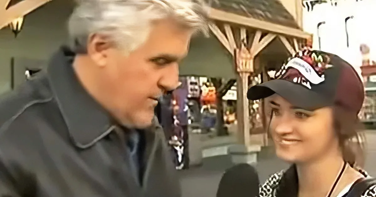 A man in a dark coat and a woman in a baseball cap are engaged in conversation, with a blurred background of a store.