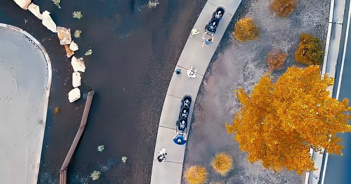 Aerial view of a sidewalk with people pushing strollers and a park area with rocks and bushes.