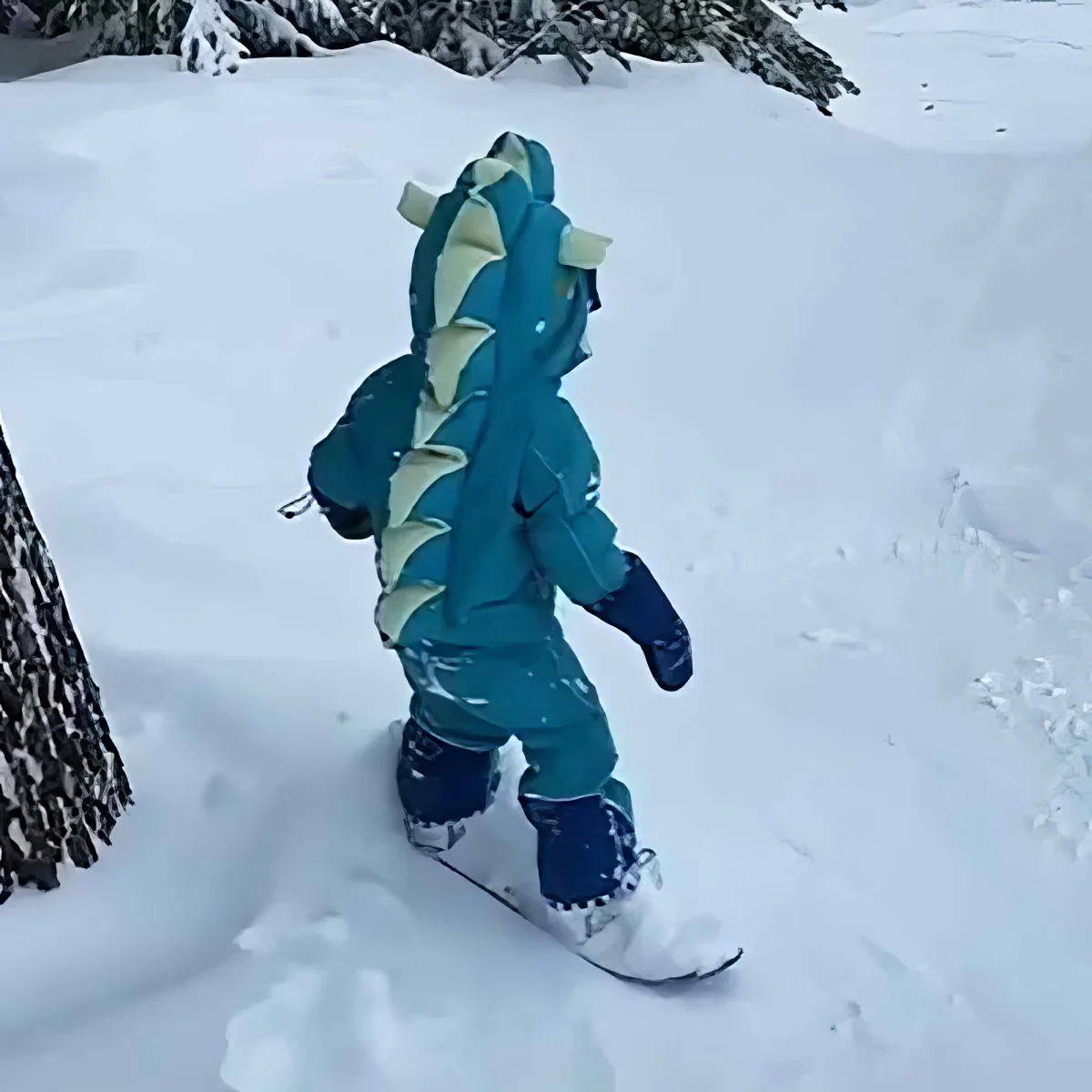 A child in a blue dragon costume walks through deep snow, surrounded by snowy trees.