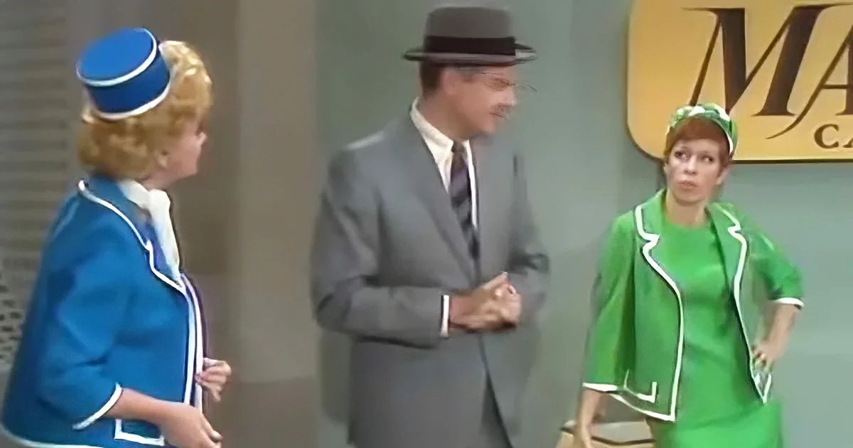 A man in a gray suit and hat stands between two women in flight attendant uniforms, one in blue and the other in green.
