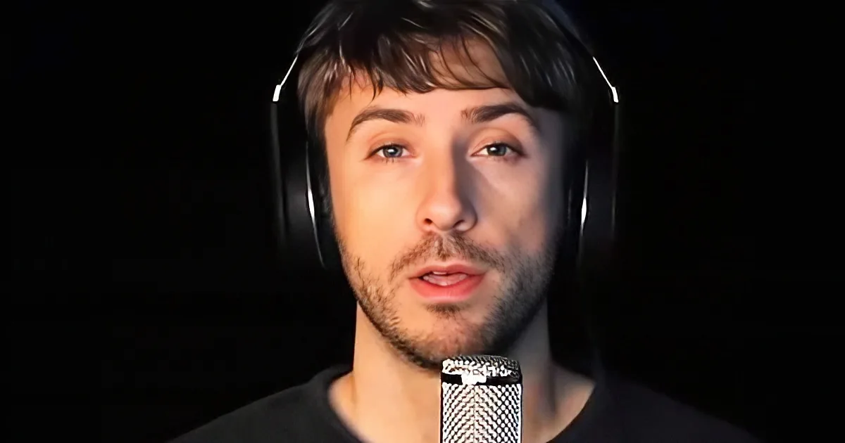 A person wearing headphones and a black shirt is speaking into a microphone against a dark background.