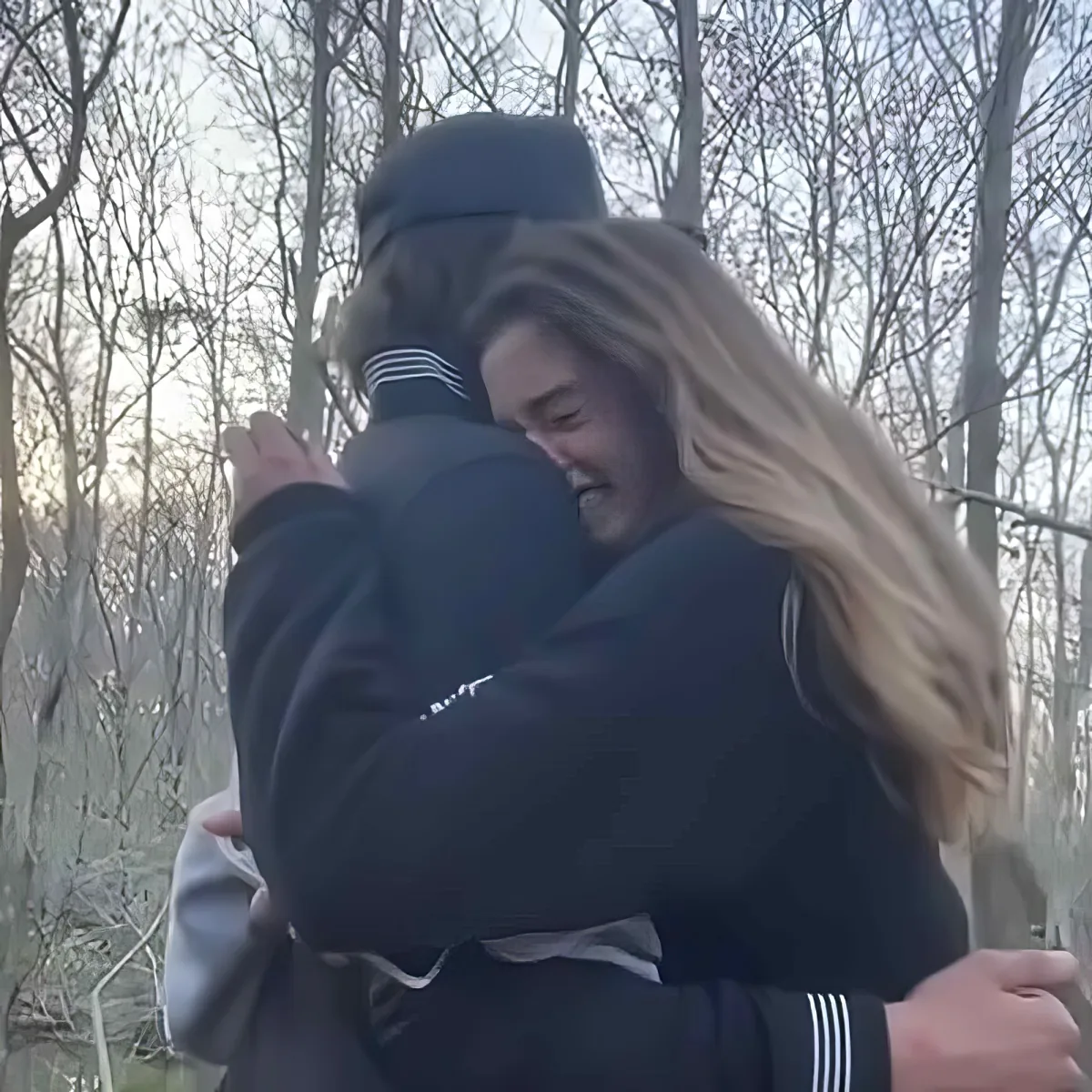 Two people in black jackets hug warmly in a forest setting.