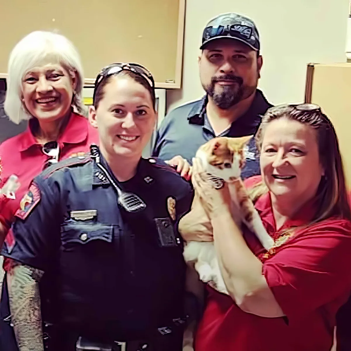 A police officer poses with a woman holding a cat, surrounded by two other women in red shirts.