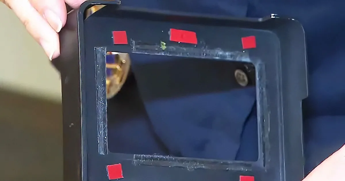 A person holds a black rectangular object with red markings, revealing a metallic interior.