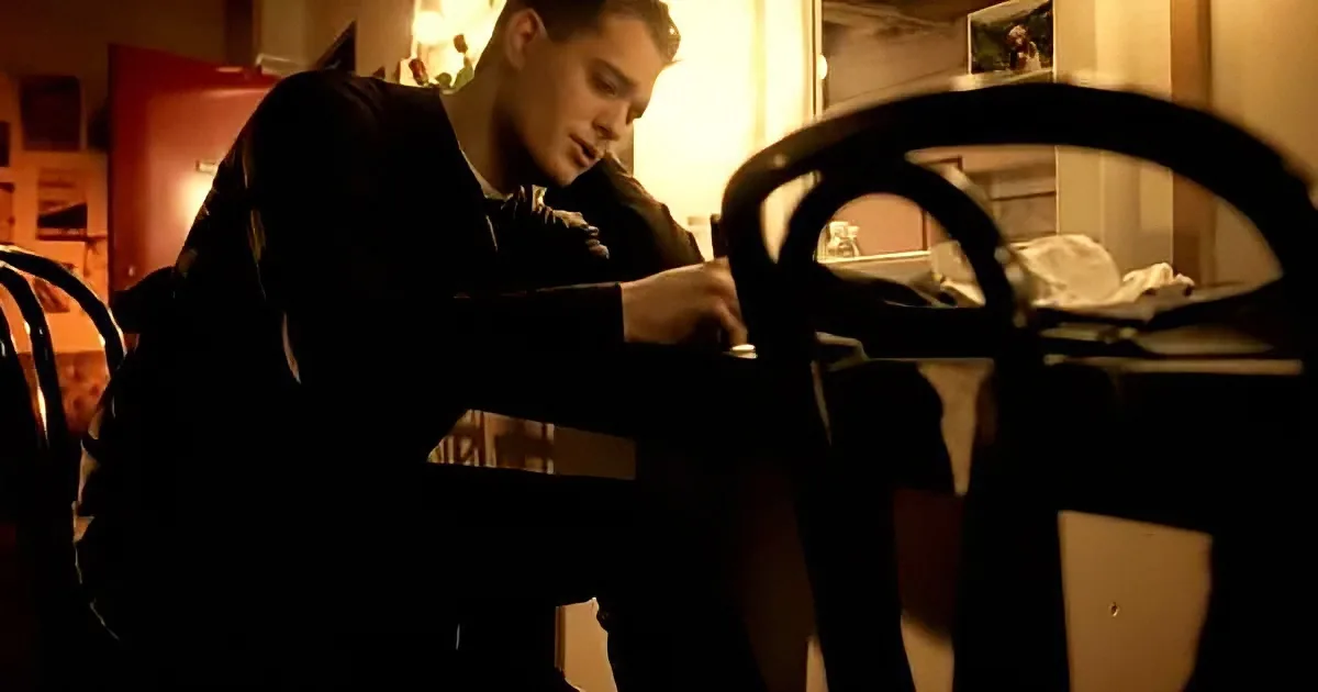 A man in a dark shirt is sitting at a table, working on something with his hands.