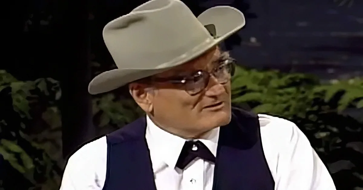 A man in a white shirt, dark vest, and white cowboy hat is looking to the side.