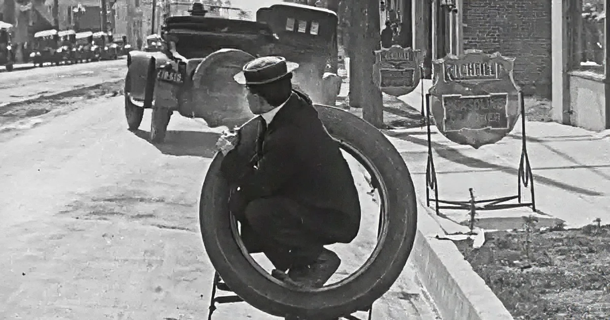 A man sits inside a large tire, surrounded by vintage gas station signs on a city street.