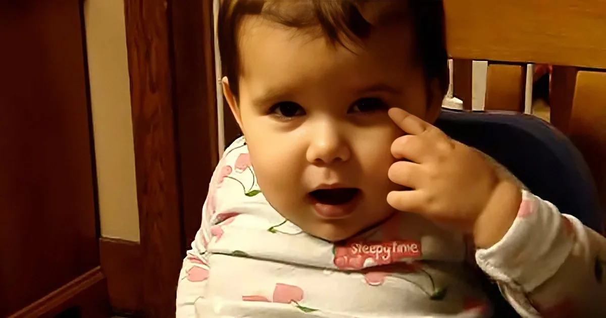 A baby in pajamas with a "Sleepy Time" bib, holding their hand to their face, looking surprised.