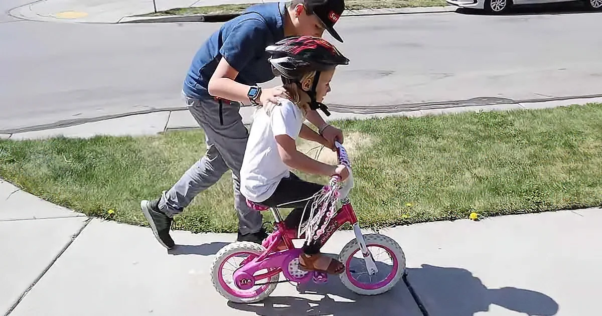 Brother teaches little sister to ride a bike
