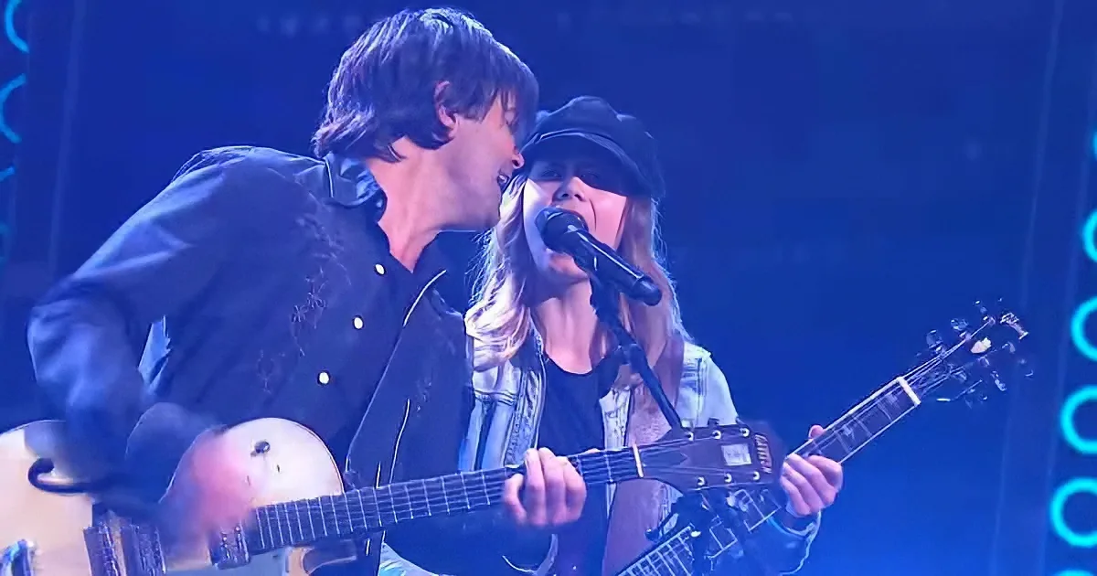 A man and woman are performing on stage, the man playing guitar and the woman singing into a microphone.
