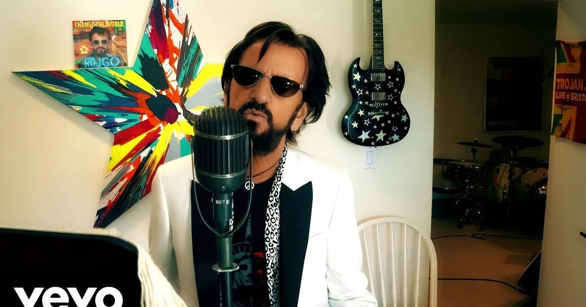 A man wearing sunglasses and headphones smiles while playing drums in a colorful room.