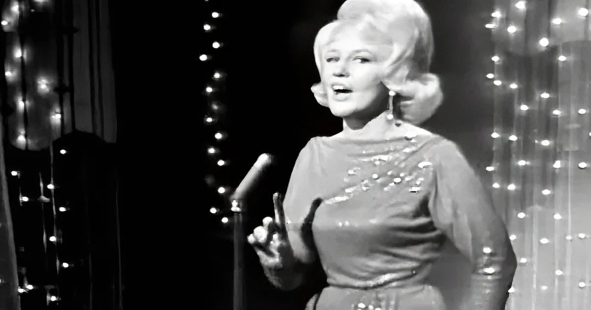 A woman in a sparkly dress sings into a microphone, surrounded by twinkling lights.
