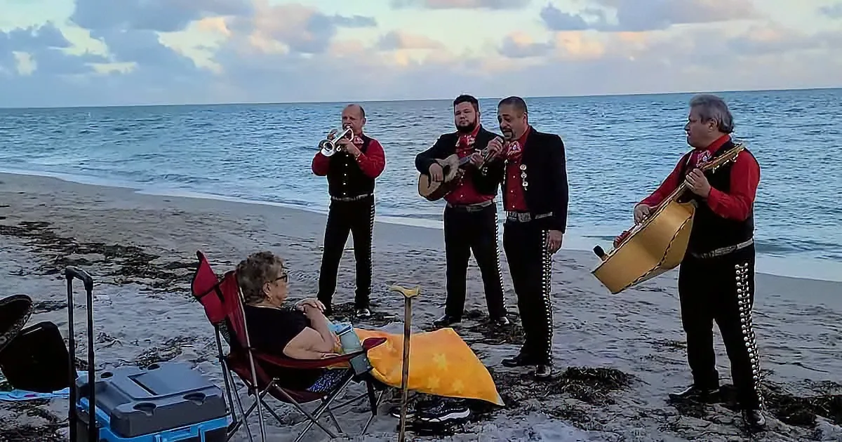 A mariachi band plays on the beach as a woman sits in a chair nearby.