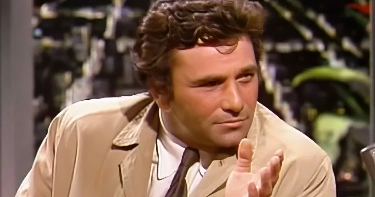 A man in a beige suit jacket and tie is gesturing with his hands while speaking.