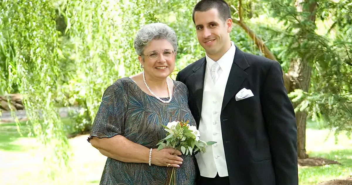 A woman in a patterned dress holds a bouquet, standing next to a man in a suit in a lush, green park.