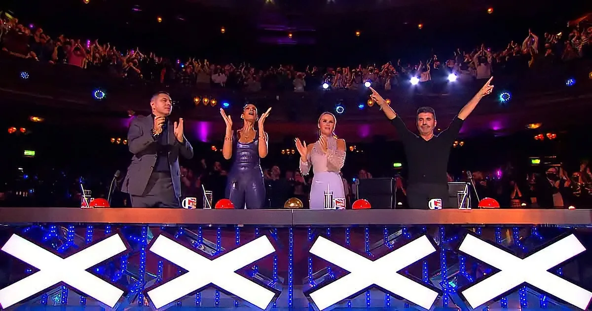 Four judges on stage with arms raised, audience cheering in the background.