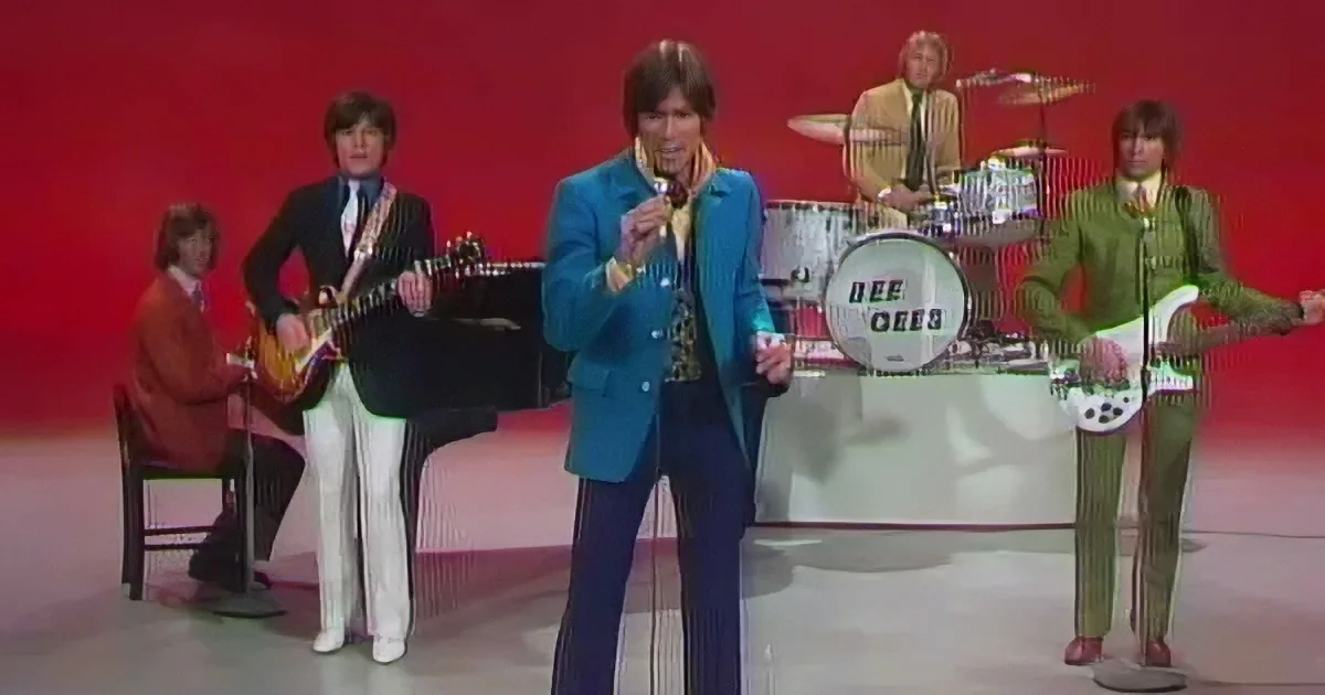 A man in a blue suit sings on stage with a band in colorful outfits.