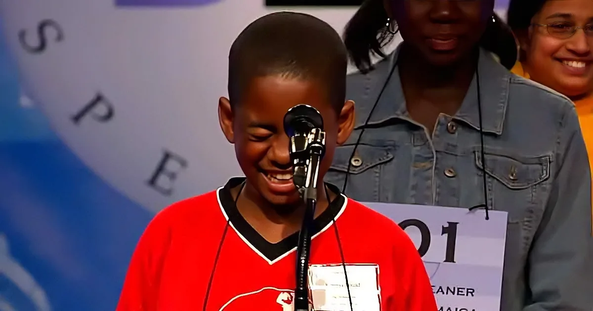 A young boy in a red shirt smiles while speaking into a microphone at a competition.