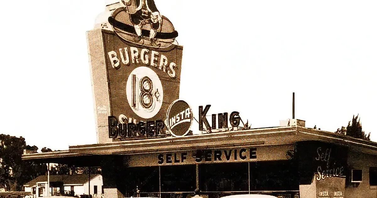 A Burger King sign with a mascot and a girl eating a Whopper with a crown on her head.