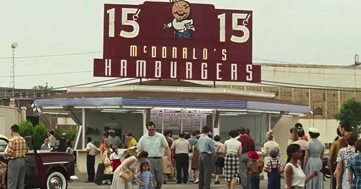 A vintage McDonald's sign advertises hamburgers for 15 cents, with people lining up in front of the drive-thru.