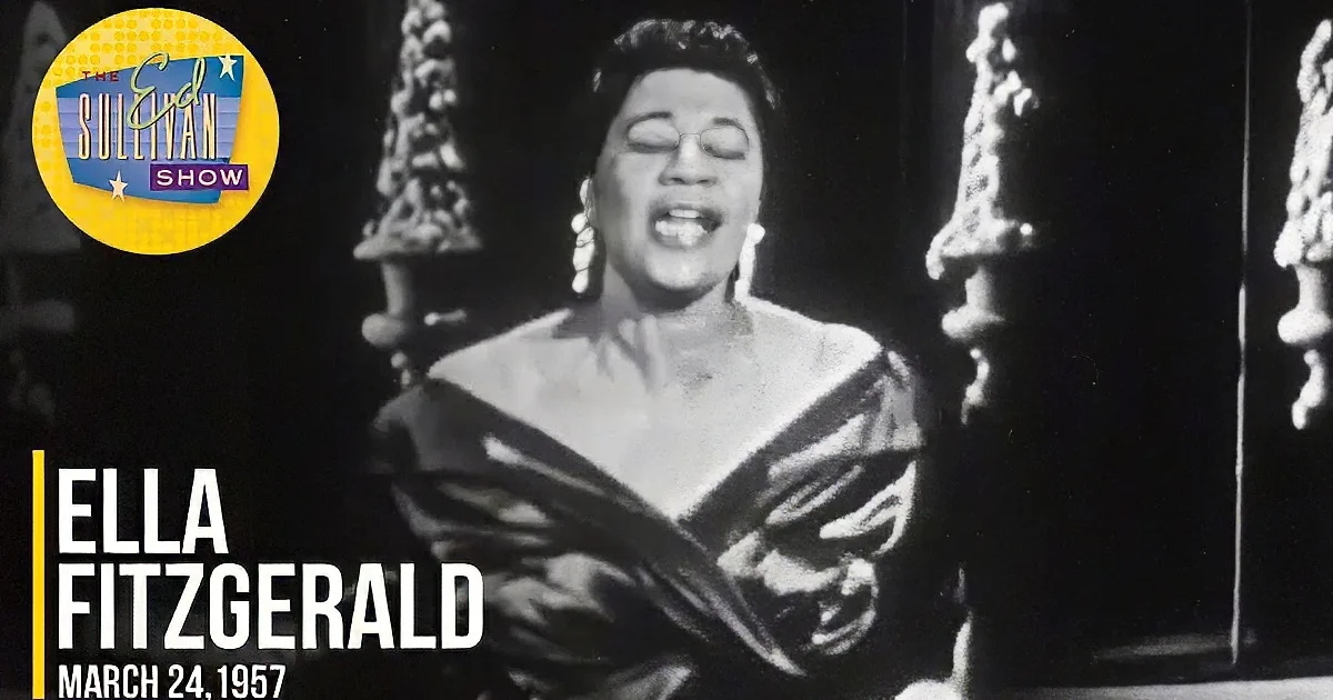 A woman in a dramatic pose, wearing a flowing dress, singing passionately in front of a window.