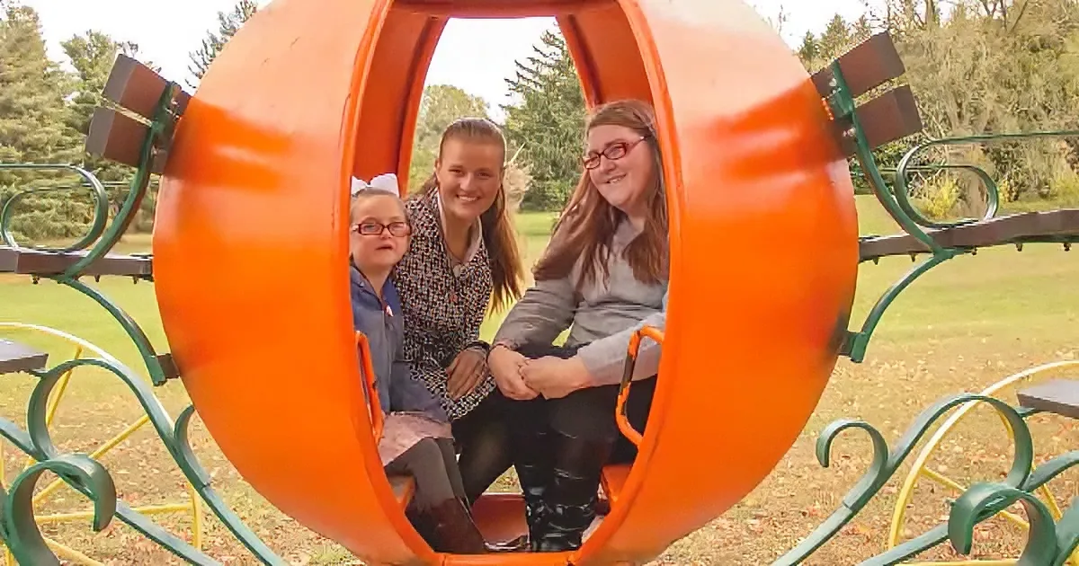 Three individuals are seated inside a large orange playground tunnel, smiling and enjoying the moment.