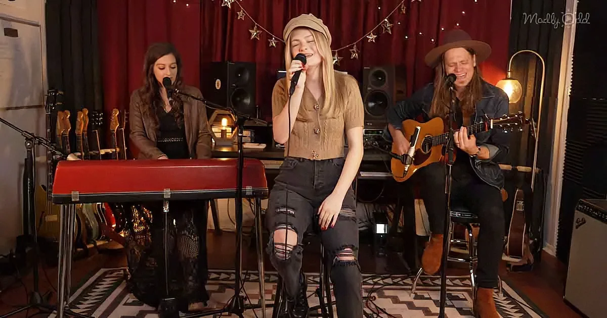 A woman sings into a microphone while playing a keyboard, accompanied by another musician playing guitar in a cozy studio...