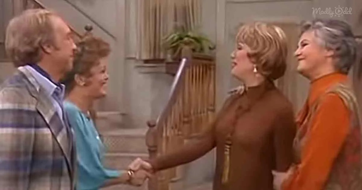 A woman in a brown turtleneck is holding a sword, while others look on in a living room setting.