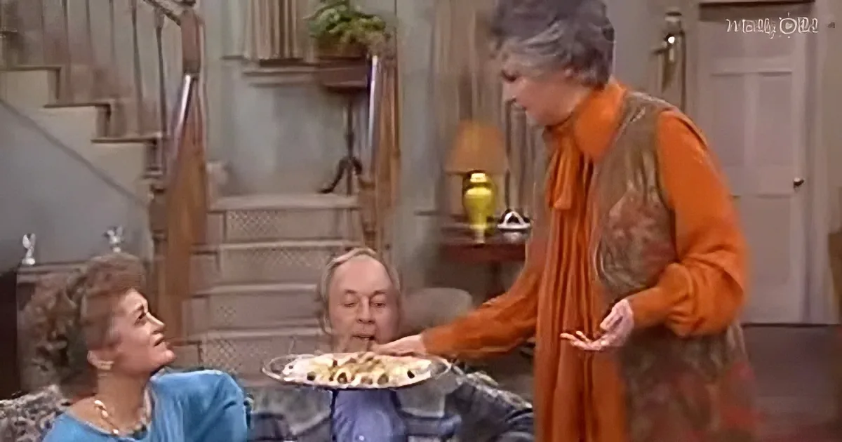 A woman in an orange outfit serves food to another woman while a third woman watches.