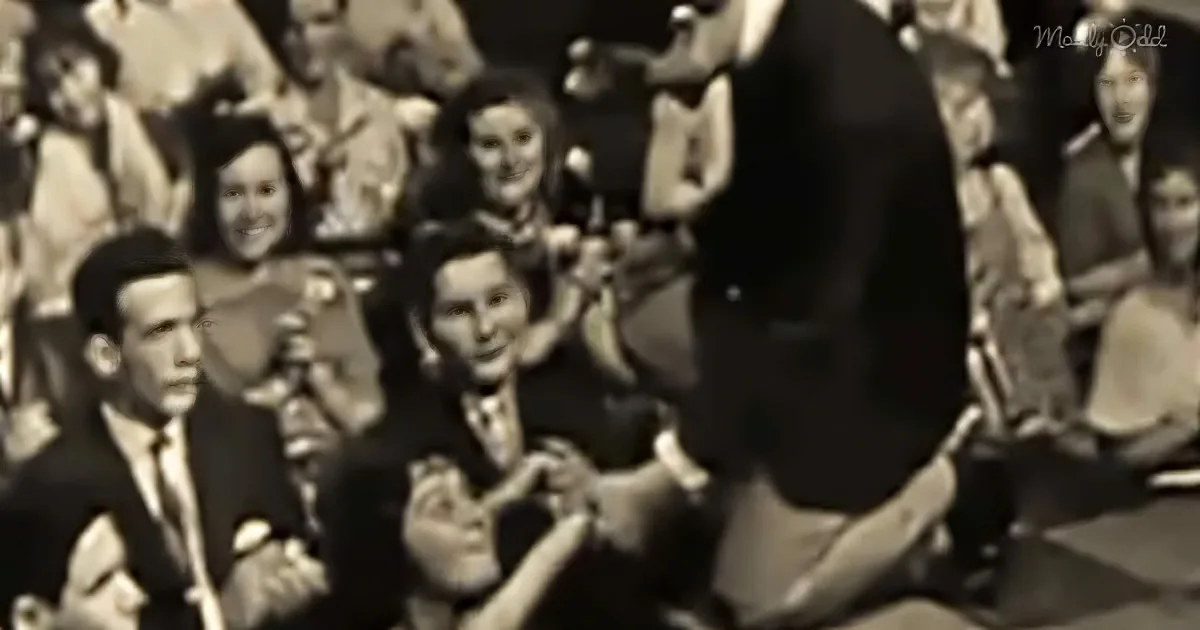 A man in a suit is surrounded by a crowd of people, some clapping and smiling.