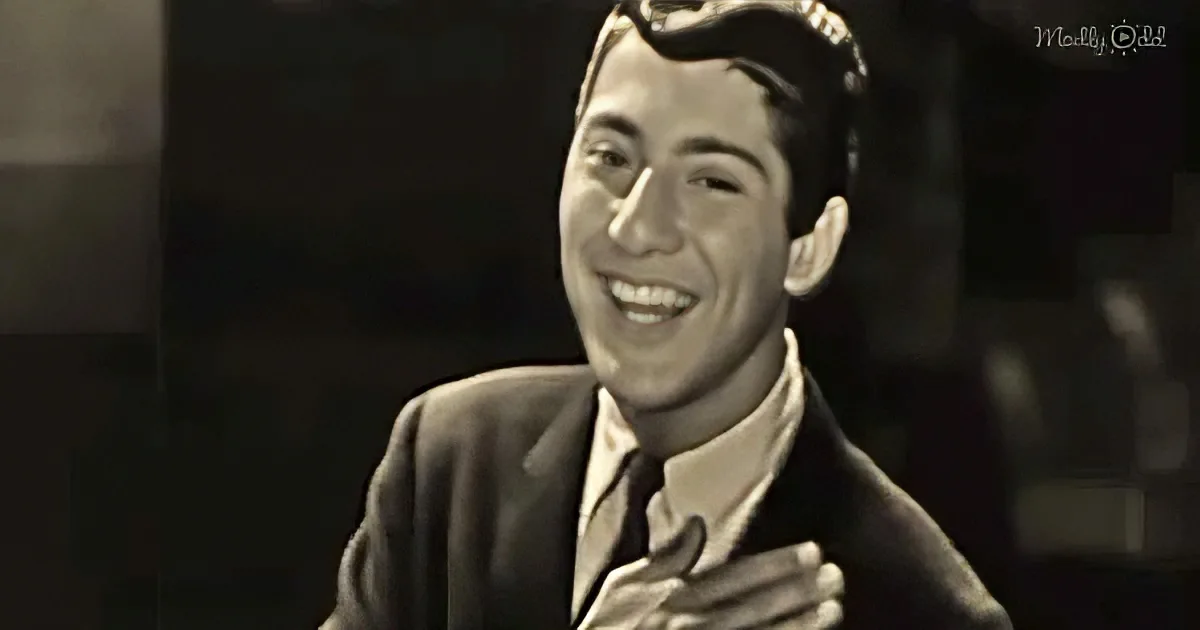 A man in a suit and tie smiles, holding his chest, in a sepia-toned image.